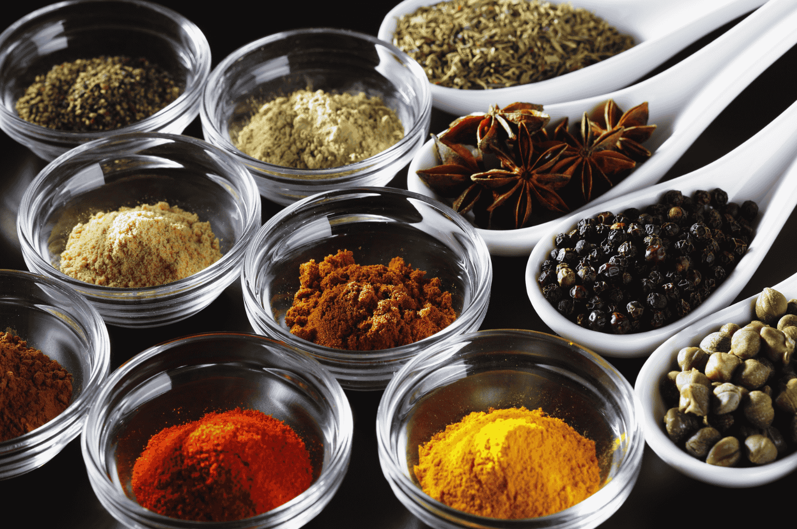 Khao-Soi-3 An overhead view of assorted spices used in crafting Khao Soi, Northern Thailand’s iconic curry noodle soup. Displayed in glass bowls and ceramic spoons, the spices include bright yellow turmeric, deep red paprika, earthy brown cumin or cinnamon, black peppercorns, green cardamom pods, star anise, and dried herbs like oregano or thyme. The colorful arrangement on a neutral surface highlights the aromatic complexity and cultural richness behind this beloved Thai dish.