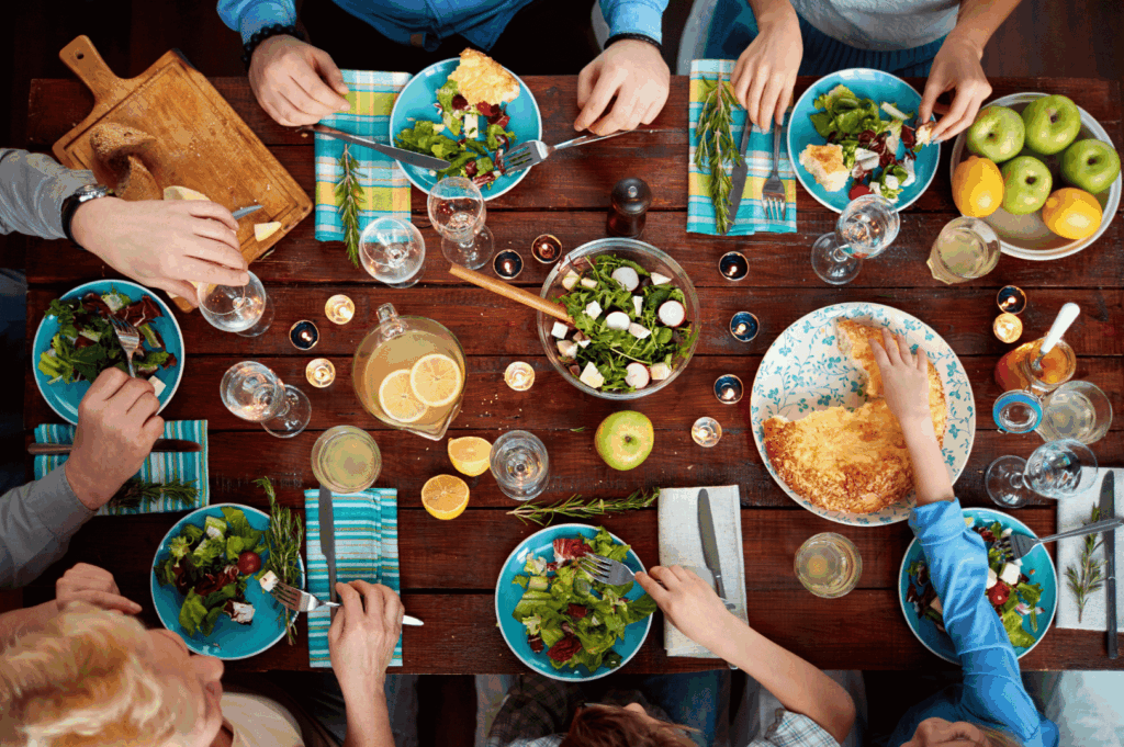 A group of people seated around a table sharing a variety of dishes, passing bowls and chatting during a communal meal.