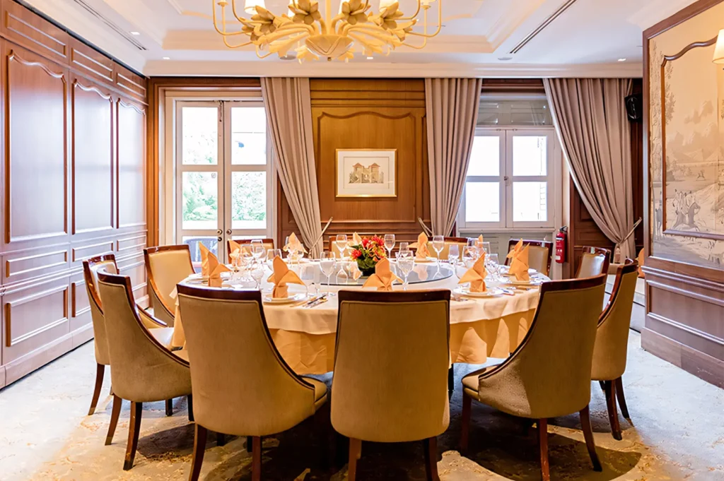 A private VIP dining room featuring a large round table with a Lazy Susan, wood-paneled walls, and elegant beige drapery.