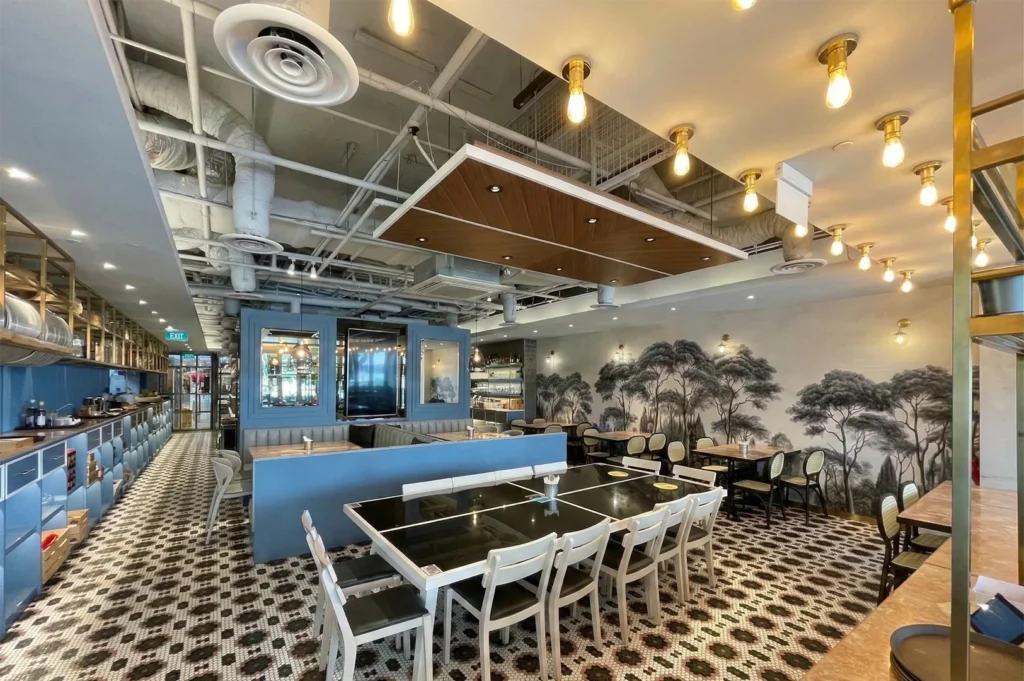A modern industrial-style bistro with a black and white mosaic tiled floor, exposed ceiling pipes, and a mural of pine trees.