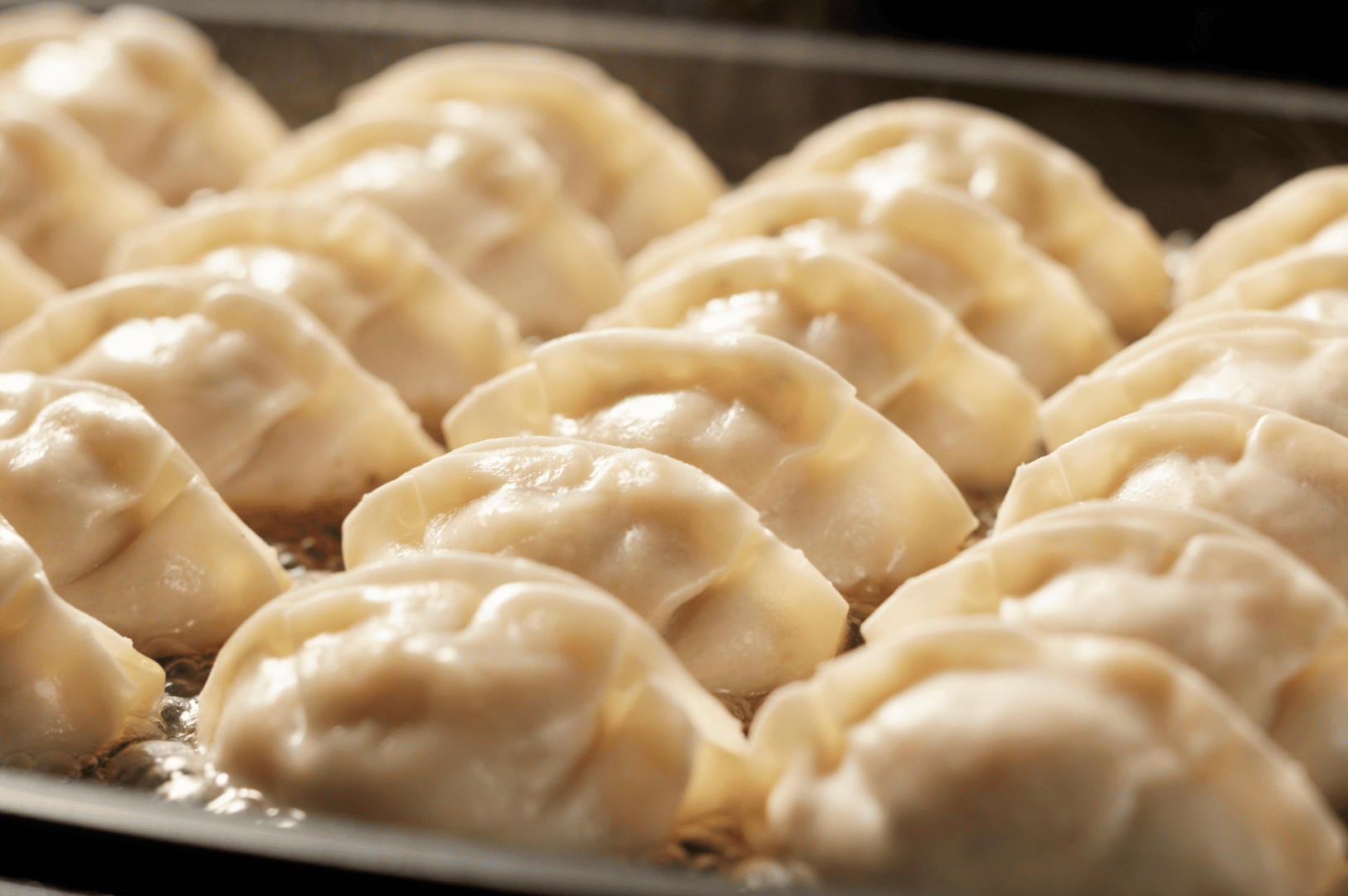 Century-Dumplings- (2) Close-up of hand-folded dumplings sizzling in bubbling oil on a pan, their pleated edges glistening with fresh dough. The rows suggest a practiced rhythm, echoing century-old techniques passed down through generations. The golden sheen and precise folds reflect the fusion of ancestral wisdom with modern culinary precision.