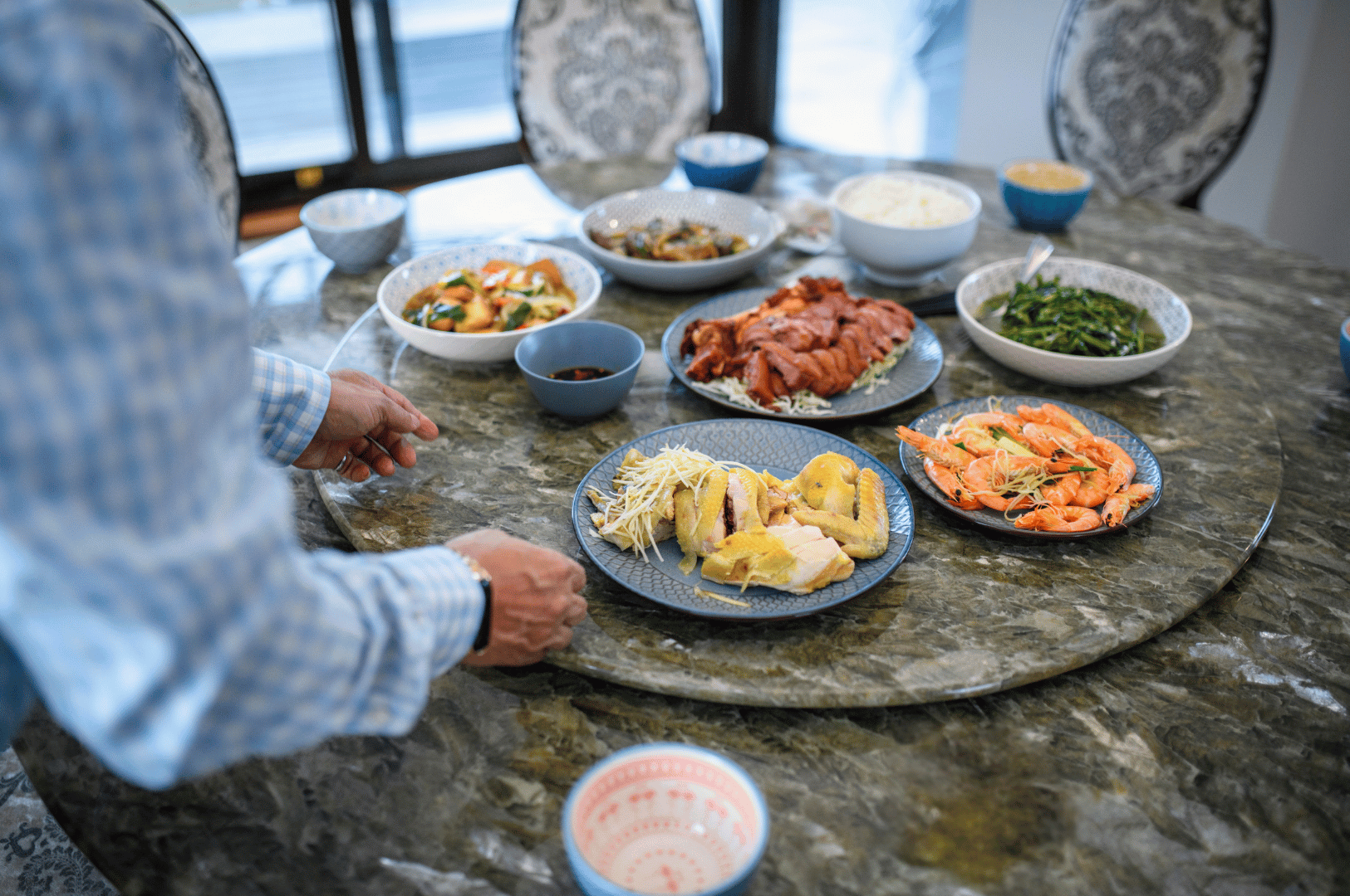 Communal-Dining- (2) Close-up of a shared meal with multiple plates and a diner reaching in, reflecting Asian traditions of togetherness around food.