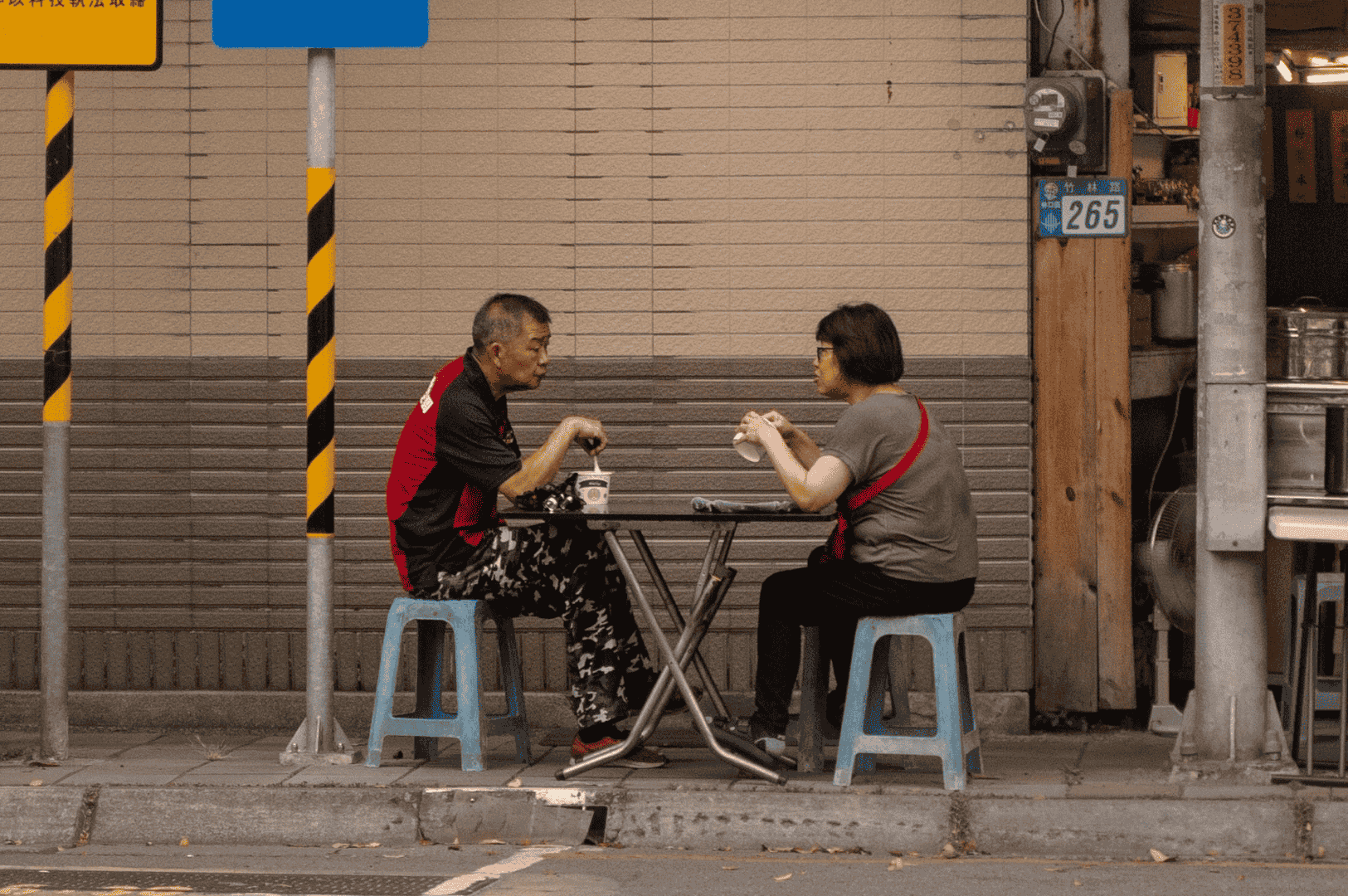 Communal-Dining- (3) Two people sharing a meal at a small street-side restaurant, symbolizing communal dining and connection in Asian food culture.