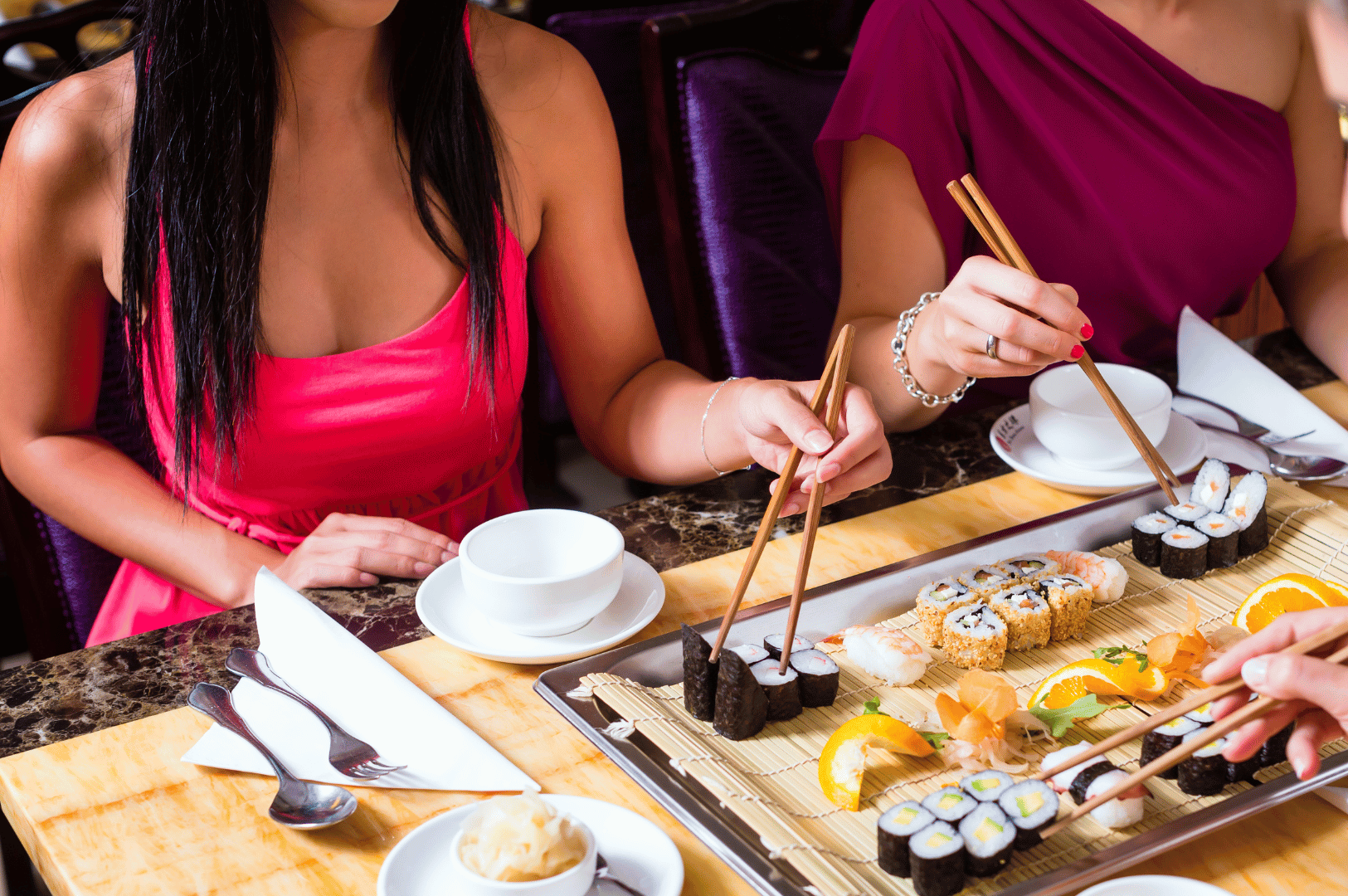 Communal-Dining- (5) Three friends sharing sushi at a table, using chopsticks and smiling—an intimate moment of communal dining in an Asian setting
