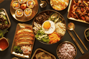 A vibrant spread of Korean side dishes and bibimbap ingredients arranged in gleaming gold trays on a patterned table, highlighting Jeonju’s rich culinary presentation.