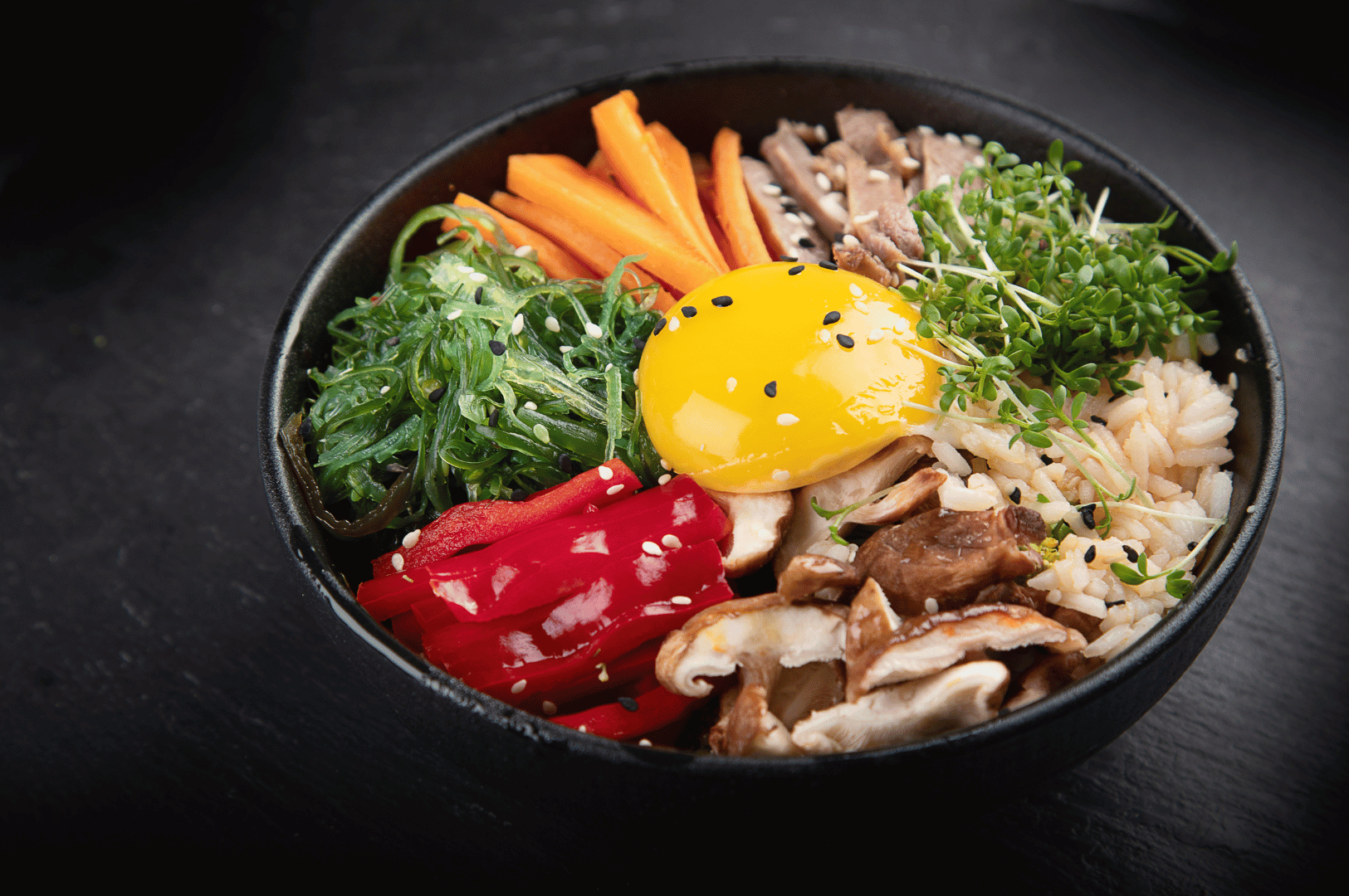 Jeonju- (4) A vibrant bowl of Jeonju-style bibimbap with steamed rice topped with sautéed vegetables, seasoned beef, and a sunny-side egg, served in a ceramic bowl on a wooden table