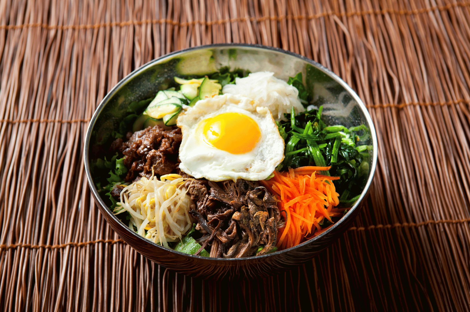 Jeonju- (6) Overhead shot of a Jeonju-style bibimbap bowl topped with a sunny-side egg, colorful vegetables, and rice in a stone bowl
