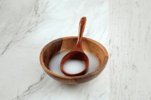 A rustic wooden bowl filled with milky-white Sikhye sweet rice punch rests on a white marble surface, evoking winter simplicity and warmth. A matching wooden ladle stands upright in the bowl, its handle leaning gently against the rim, suggesting a moment of quiet hospitality. The natural wood tones contrast with the creamy liquid, highlighting Sikhye’s comforting presence across seasonal Korean traditions.