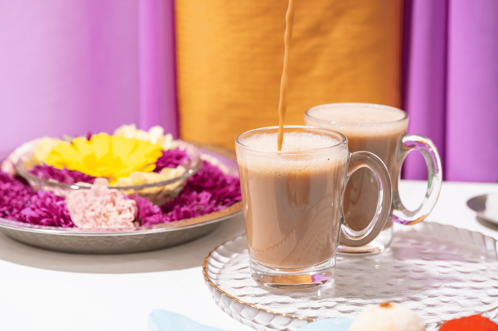 Two steaming mugs of frothy pulled tea on a rustic table, with soft florals nearby—evoking Malaysia’s beloved teh tarik ritual.