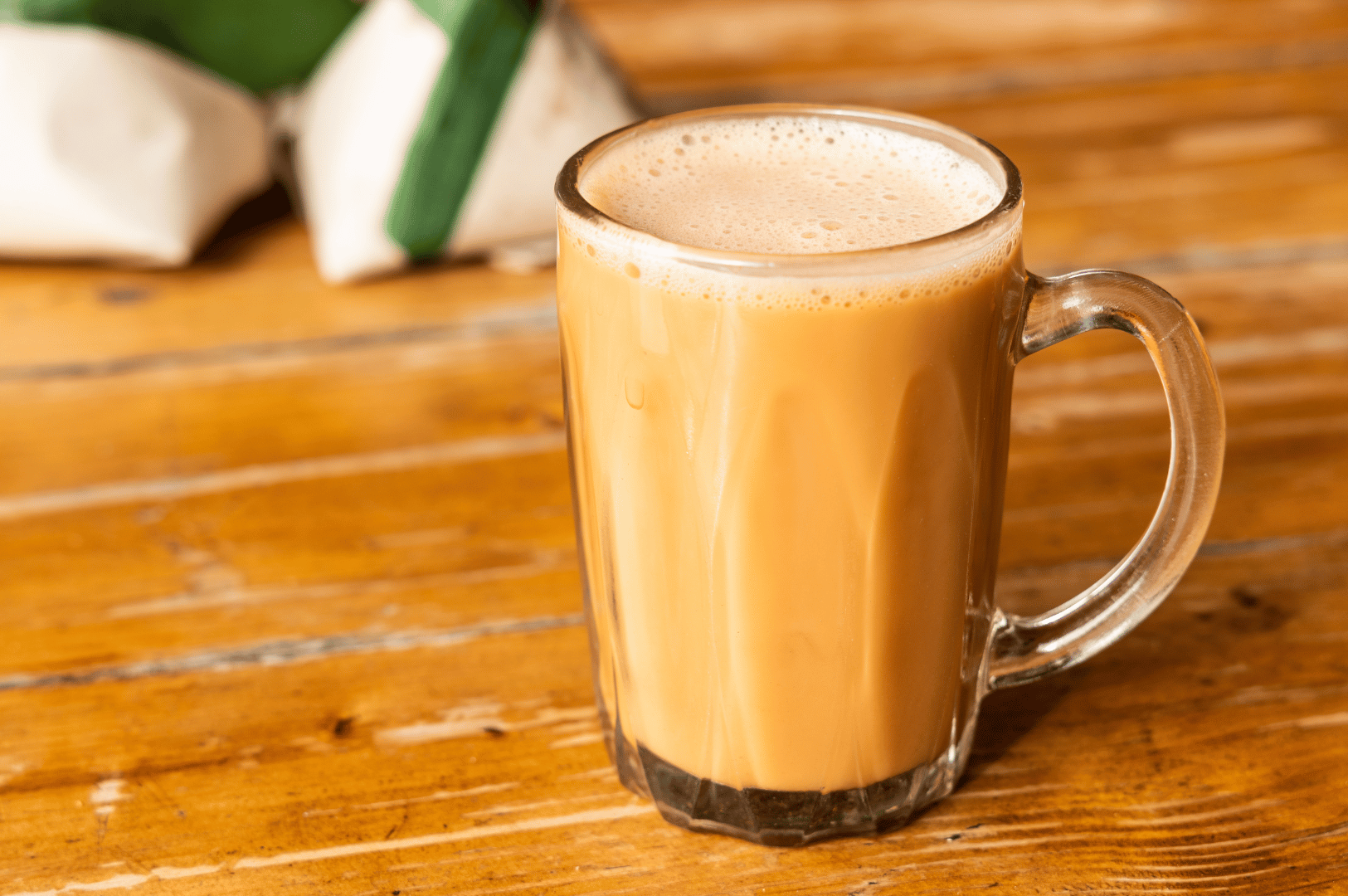 A glass of frothy teh tarik on a wooden table, captured close-up to highlight the creamy foam and caramel-brown color—perfect for a feature on Malaysia’s iconic pulled tea.