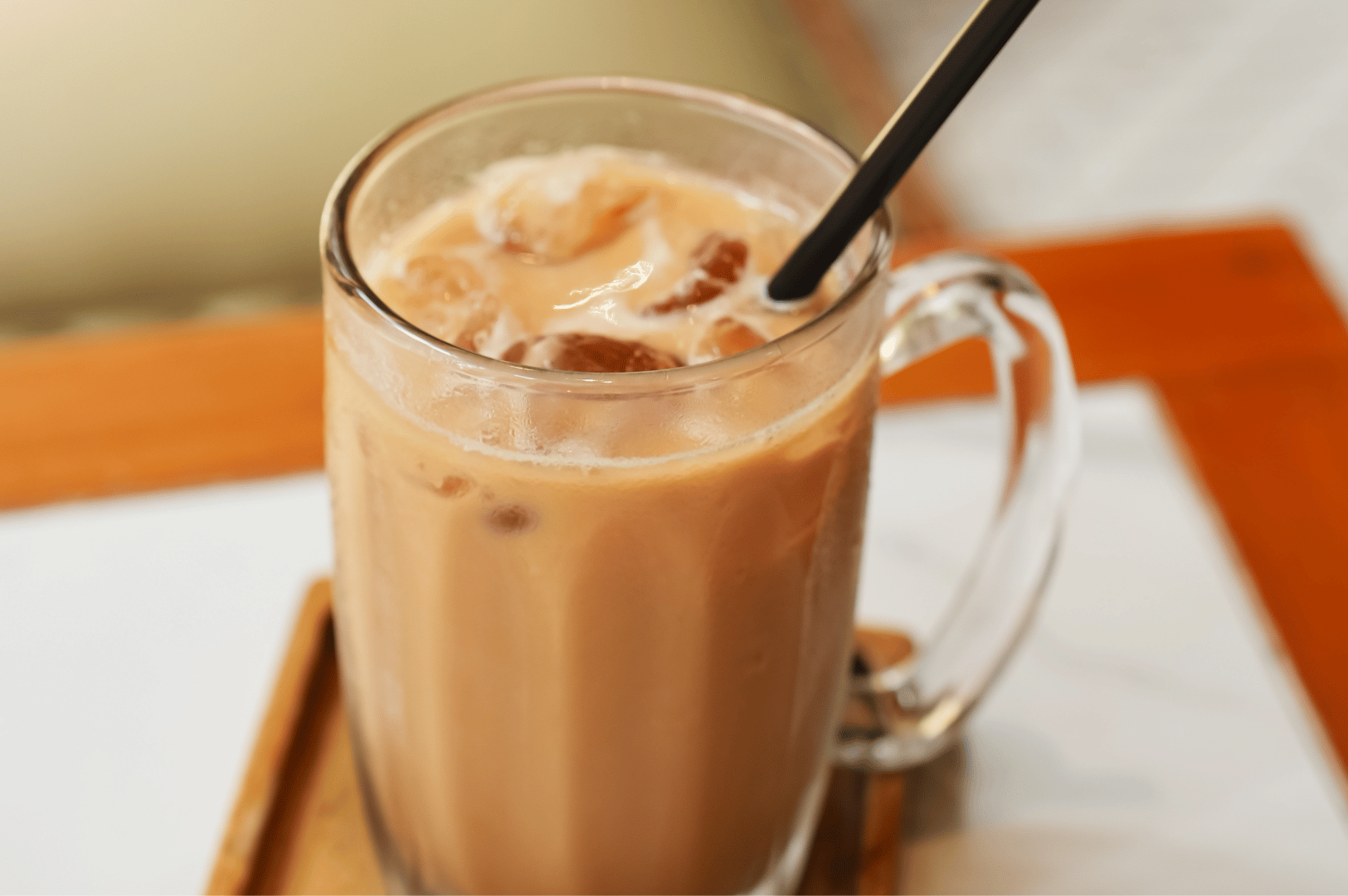 A frosty glass of iced milk tea on a wooden table, condensation visible, photographed in warm natural light — setting the scene for Malaysia’s beloved pulled tea culture.