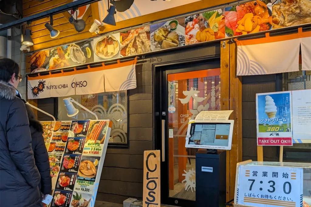 Entrance of Nijo Ichiba Ohso restaurant in Sapporo showing a digital queue kiosk and a menu board with premium King Crab and Uni dishes.
