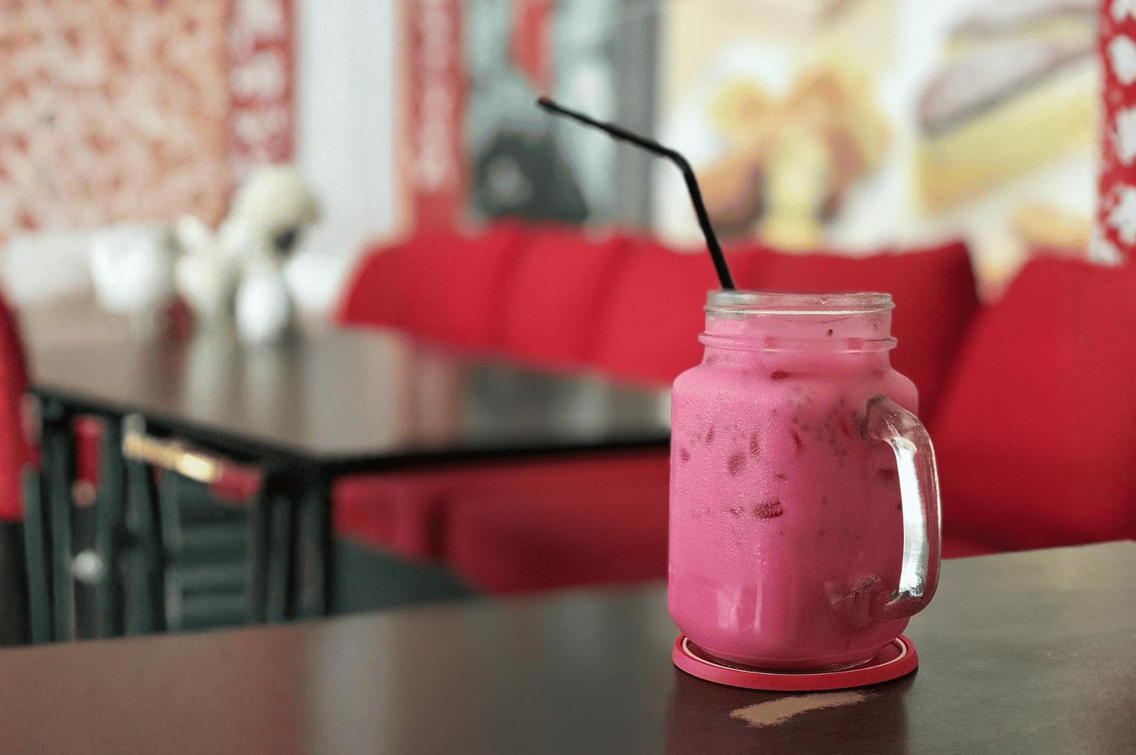 Bright pink iced Bandung drink served in a mason jar with a black straw, set on a red coaster in a vibrant café—showcasing Singapore’s beloved rose syrup milk tradition.