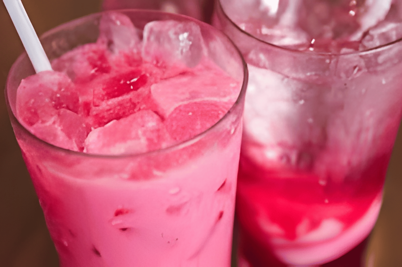 Two iced Bandung drinks—one creamy pink, one translucent red—served in chilled glasses with straws, capturing Singapore’s refreshing rose syrup milk tradition.