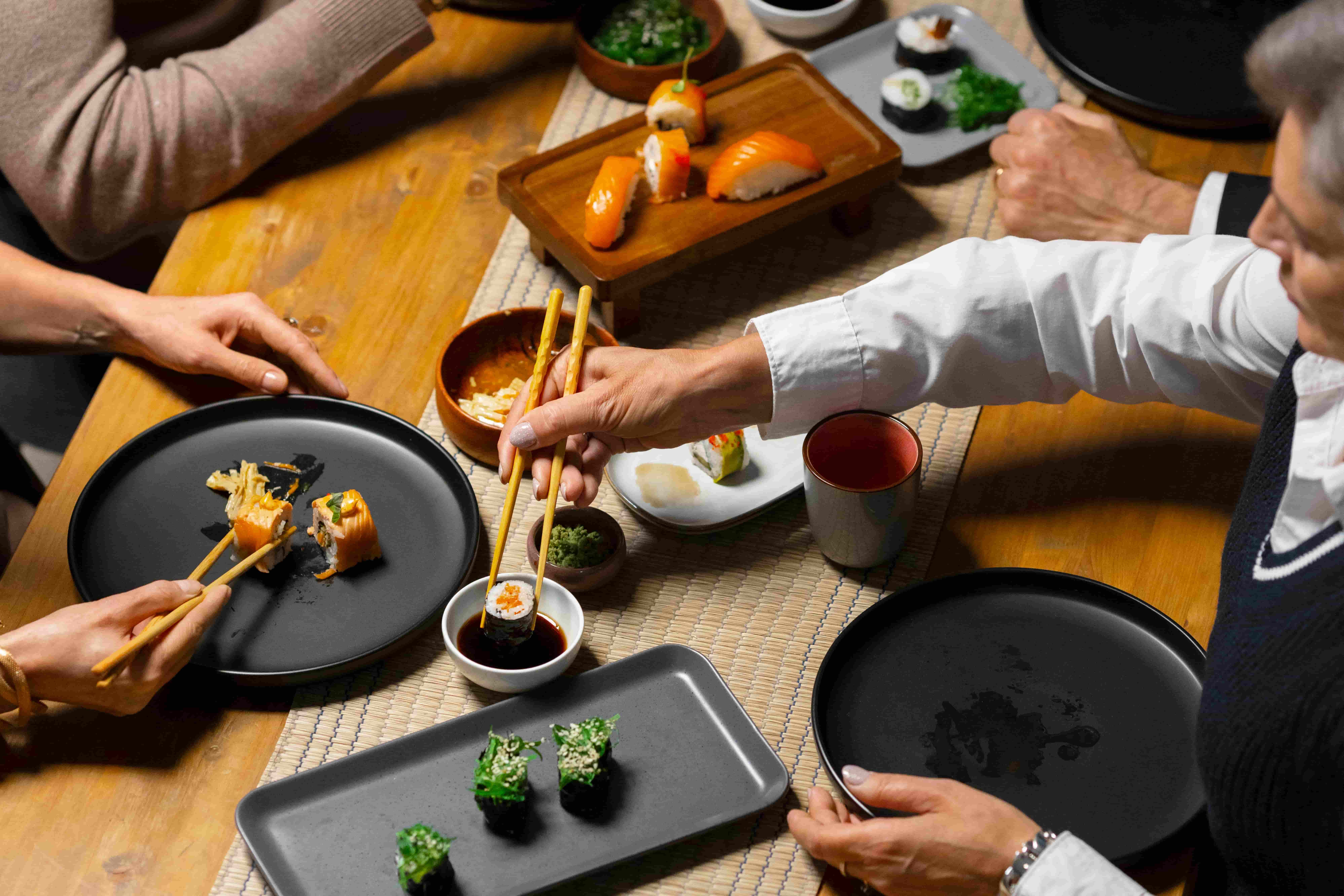 A photo of a family eating together with the woman showing the proper use of chopsticks.