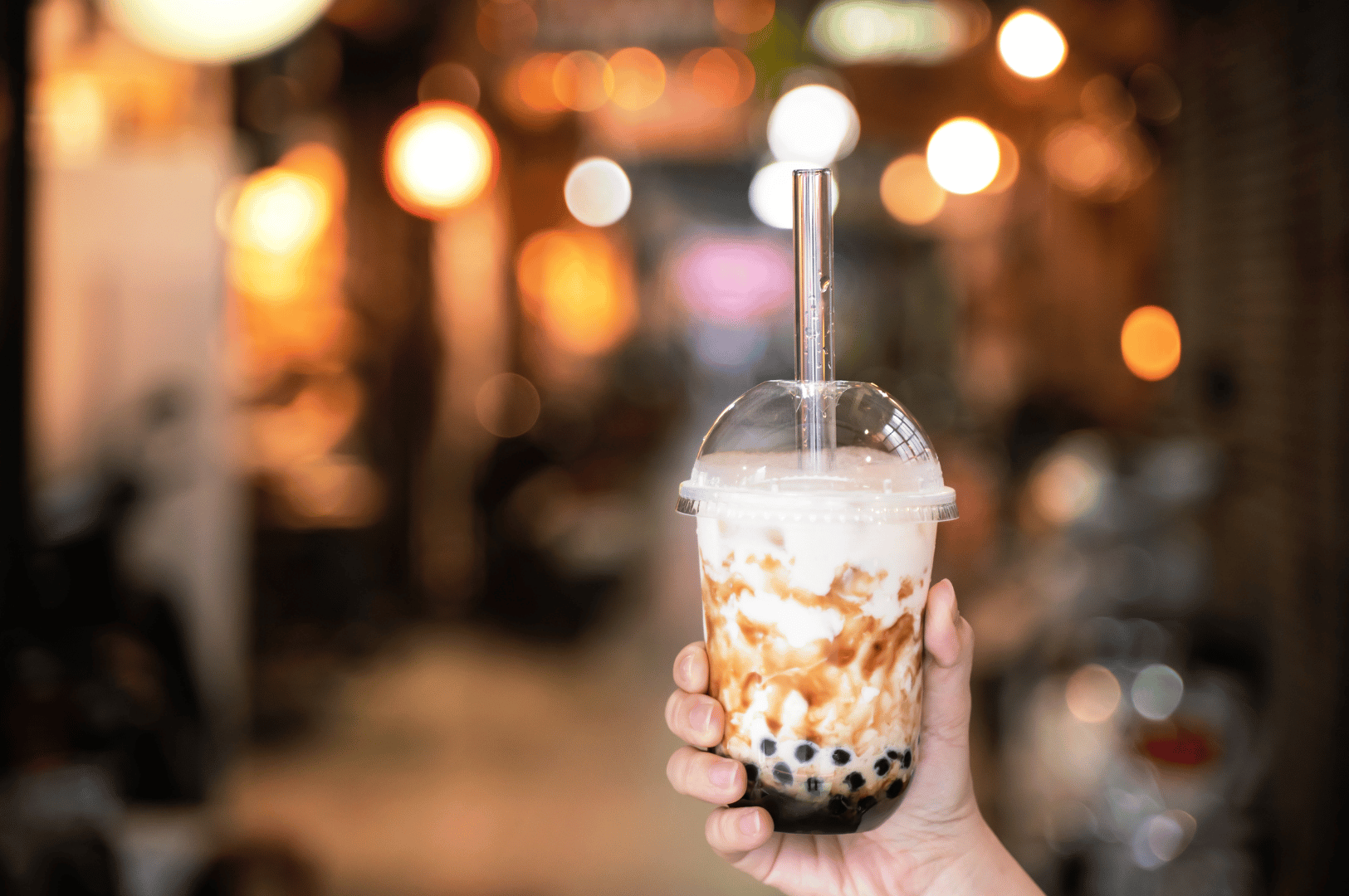 Hand holding a cup of brown sugar bubble tea with tapioca pearls in front of warm café lights, showing how Taiwan’s street drink became a global café favorite.