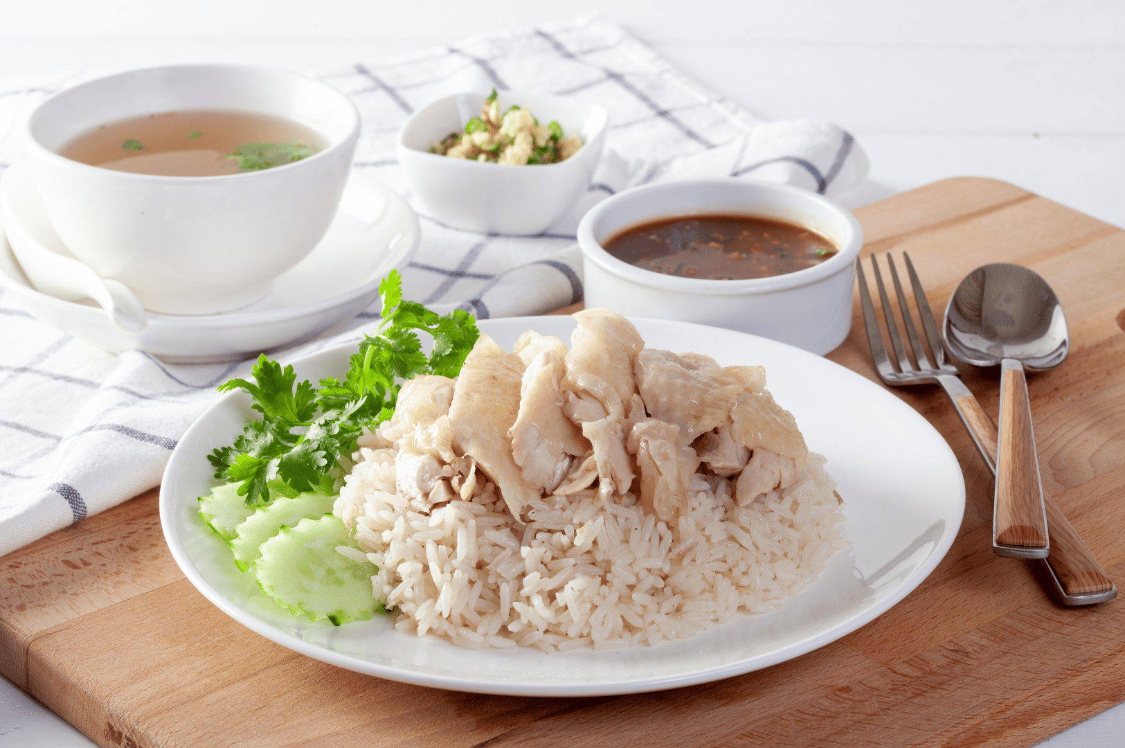 Plated Hainanese chicken rice with poached chicken, fragrant white rice, cucumber slices, and dipping sauces on a wooden board—classic Singaporean dish featured in The Ultimate Hainanese Chicken Rice Recipe: A Deep Dive.
