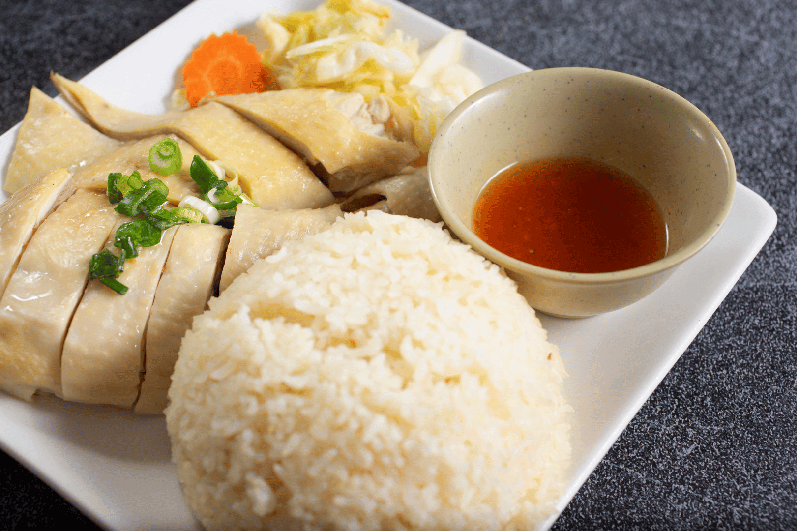 Poached chicken with scallion garnish, seasoned rice, chili sauce, and pickled vegetables—vibrant plating of Hainanese chicken rice featured in The Ultimate Hainanese Chicken Rice Recipe: A Deep Dive.