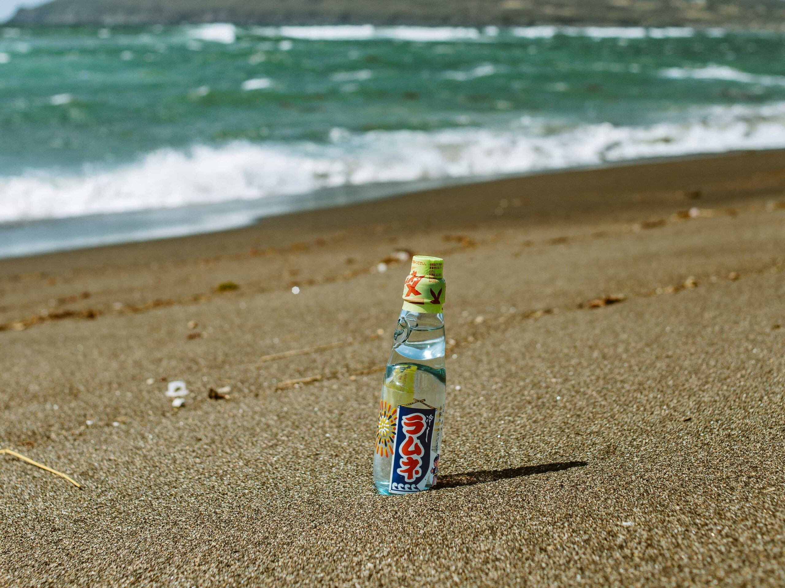 Ramune Marble Soda - 4 A rumune bottle on top of a bed of sand at the beach.