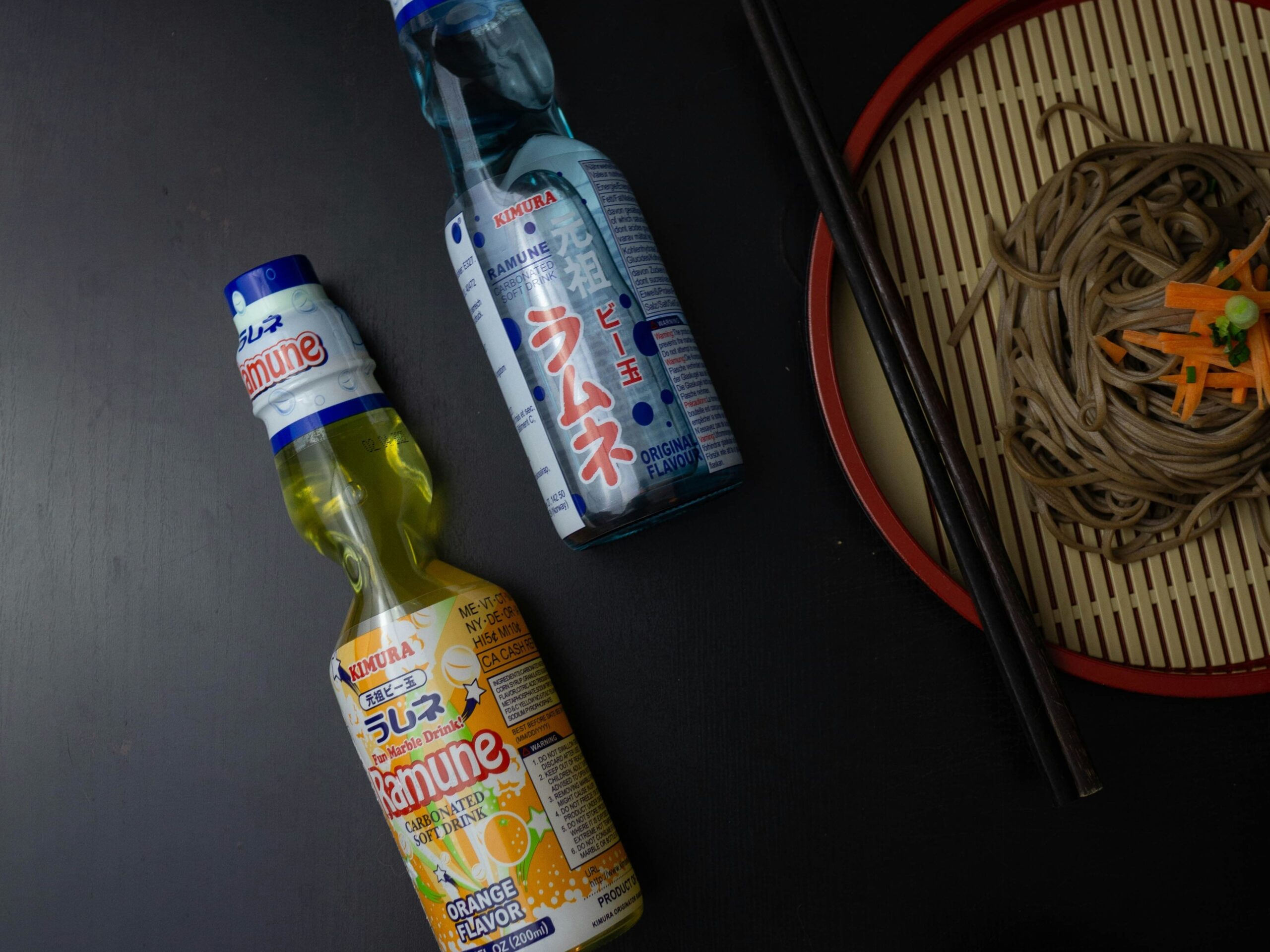 Ramune Marble Soda - 6 Ramune bottles aesthetically positioned next to a plate of noodles.