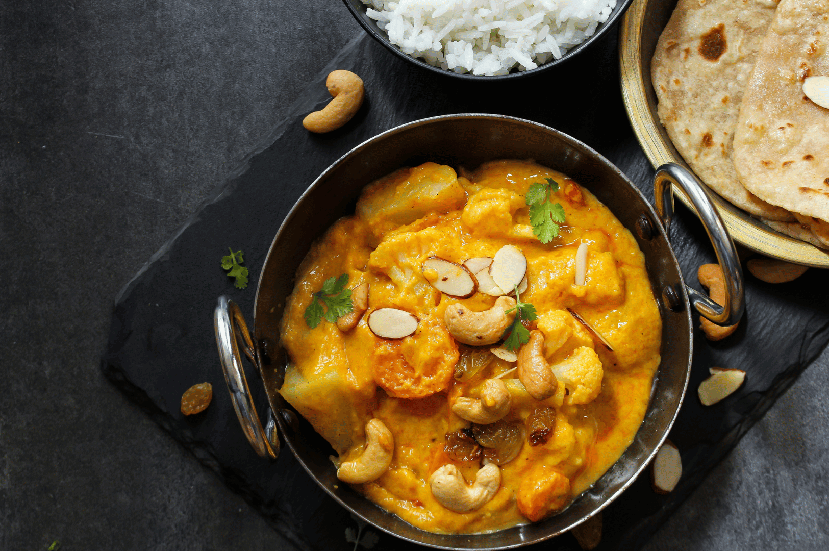 Close-up of a creamy slow-cooked curry topped with cashews, served with rice and flatbread—highlighting patient cooking in South Asian cuisine.