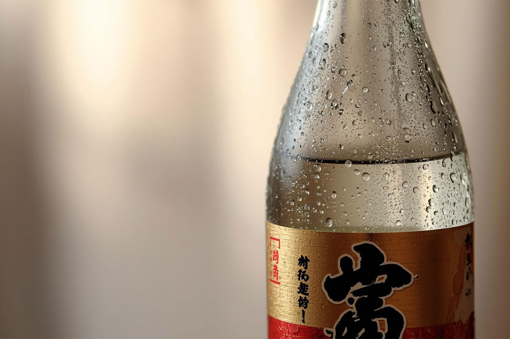 2-chilled-sake-bottle-water-droplets Close-up of a cold glass sake bottle covered in condensation and water droplets, with a gold and red label with Japanese characters.