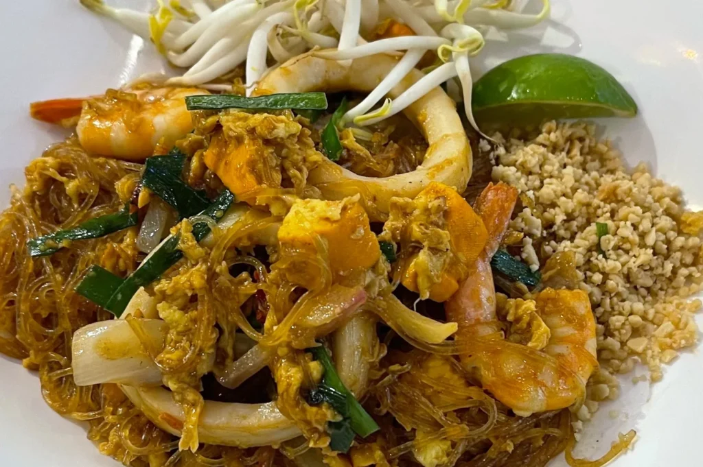 Seafood Pad Thai made with glass noodles, large shrimp, squid rings, tofu, and chives, topped with fresh bean sprouts and lime.