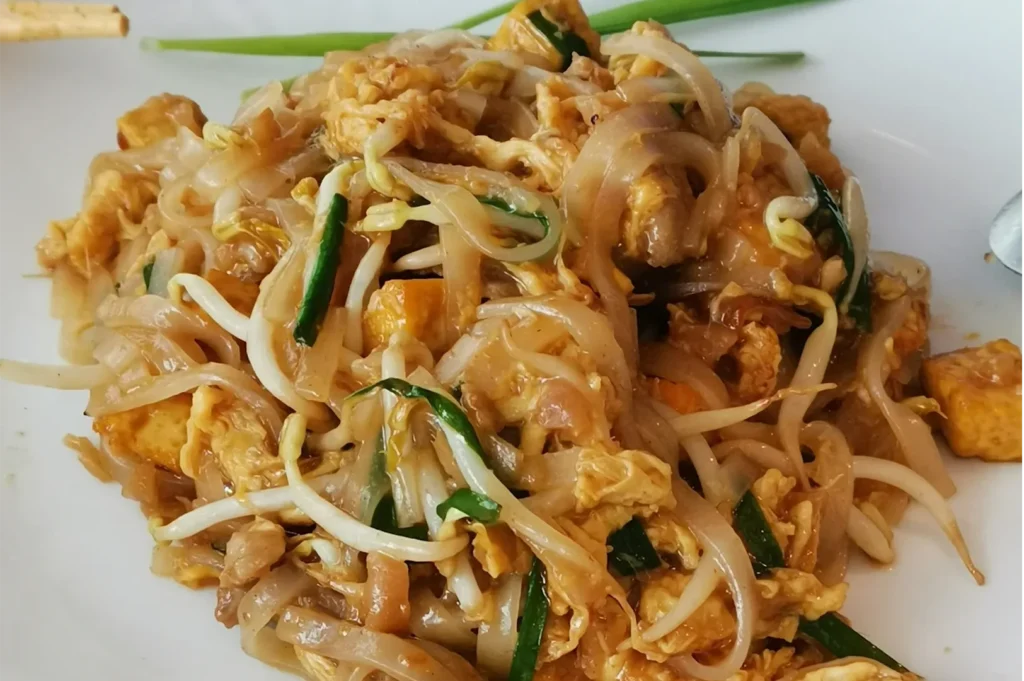 Close-up of Vegetarian Pad Thai featuring golden fried tofu cubes, fresh green chives, bean sprouts, and translucent rice noodles.