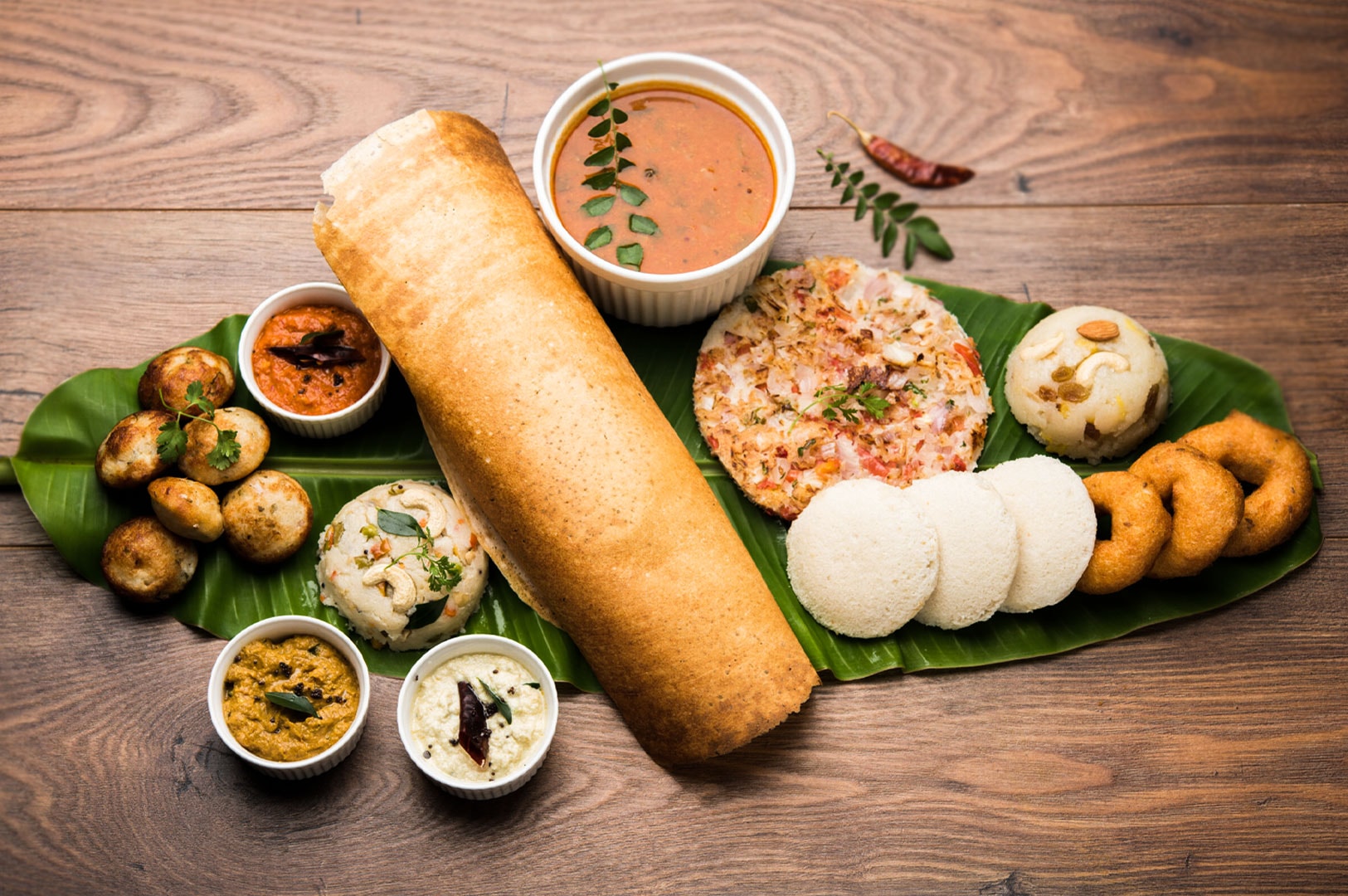 Traditional South Indian breakfast spread served on a banana leaf, featuring a large crispy dosa, soft idli, vada, upma, sambar, and coconut chutney.