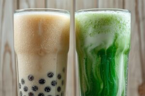 Two tall glasses of bubble tea side-by-side on a wooden surface; the left glass contains classic milk tea with tapioca pearls, and the right glass contains iced matcha green tea with milk swirls.