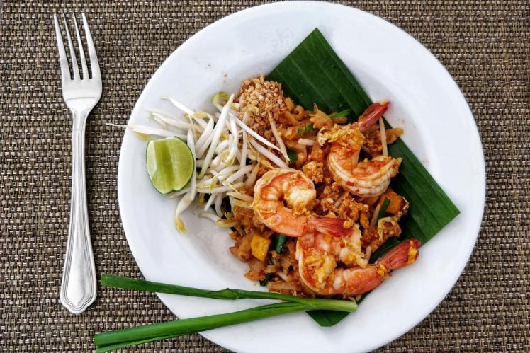 This top-down view captures a vibrant plate of shrimp Pad Thai served on a banana leaf, featuring three large prawns resting atop stir-fried noodles.