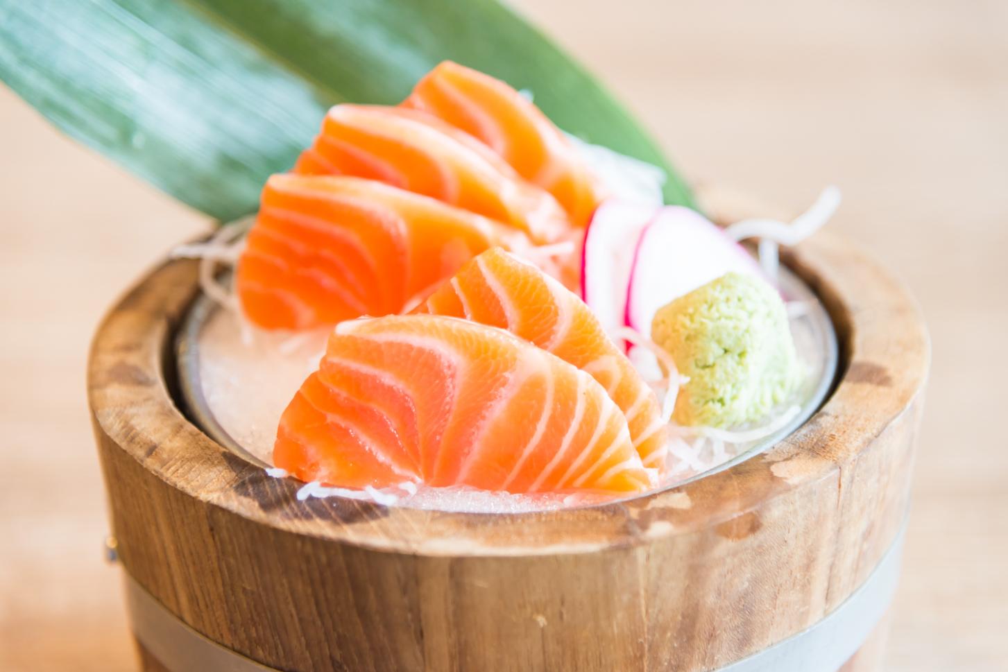 Sashimi - 1 Wooden bowl filled with fresh salmon sashimi slices on ice, served with wasabi, radish slices, and a leaf garnish.
