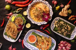An image of multiple Thai food spread across the table with spices and ingredients scattered on the black table.