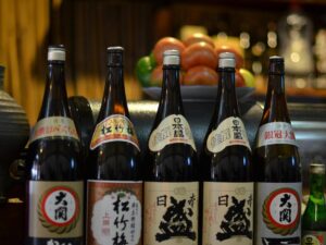 An elegant display of traditional sake bottles next to each other on a countertop surrounded by fruits and other drinks.