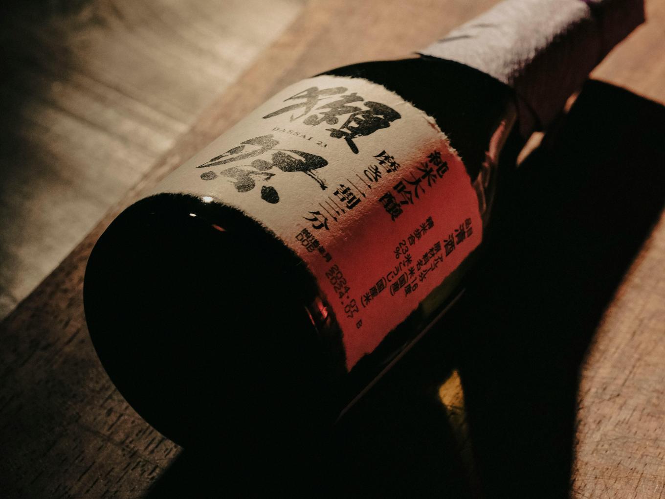 Understanding Sake - 7 A close-up photo of a sake bottle as it lays on a wooden board with strong lighting that highlights its name.