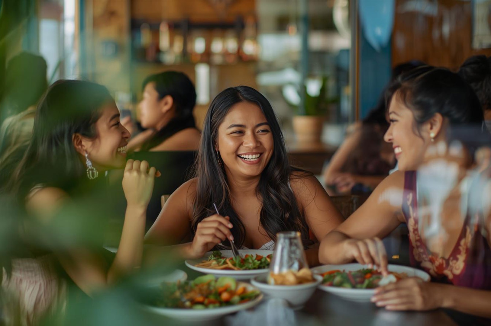 Three young women smiling and enjoying a meal together at a brightly lit indoor restaurant, with focus on the woman in the center.