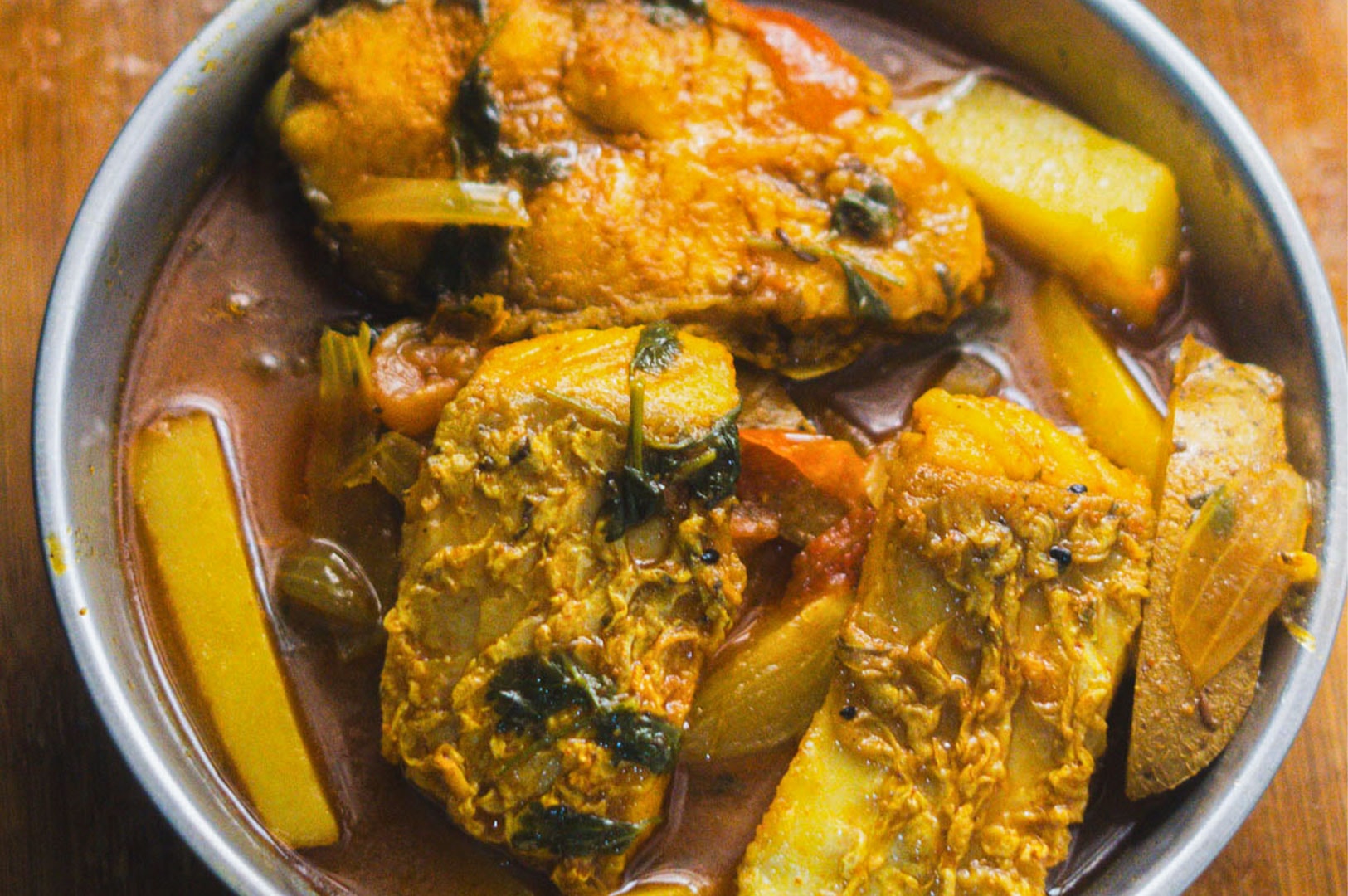 A bowl of spicy Indian fish curry cooked with potatoes in a reddish tomato-based gravy, also known as Machher Jhol.