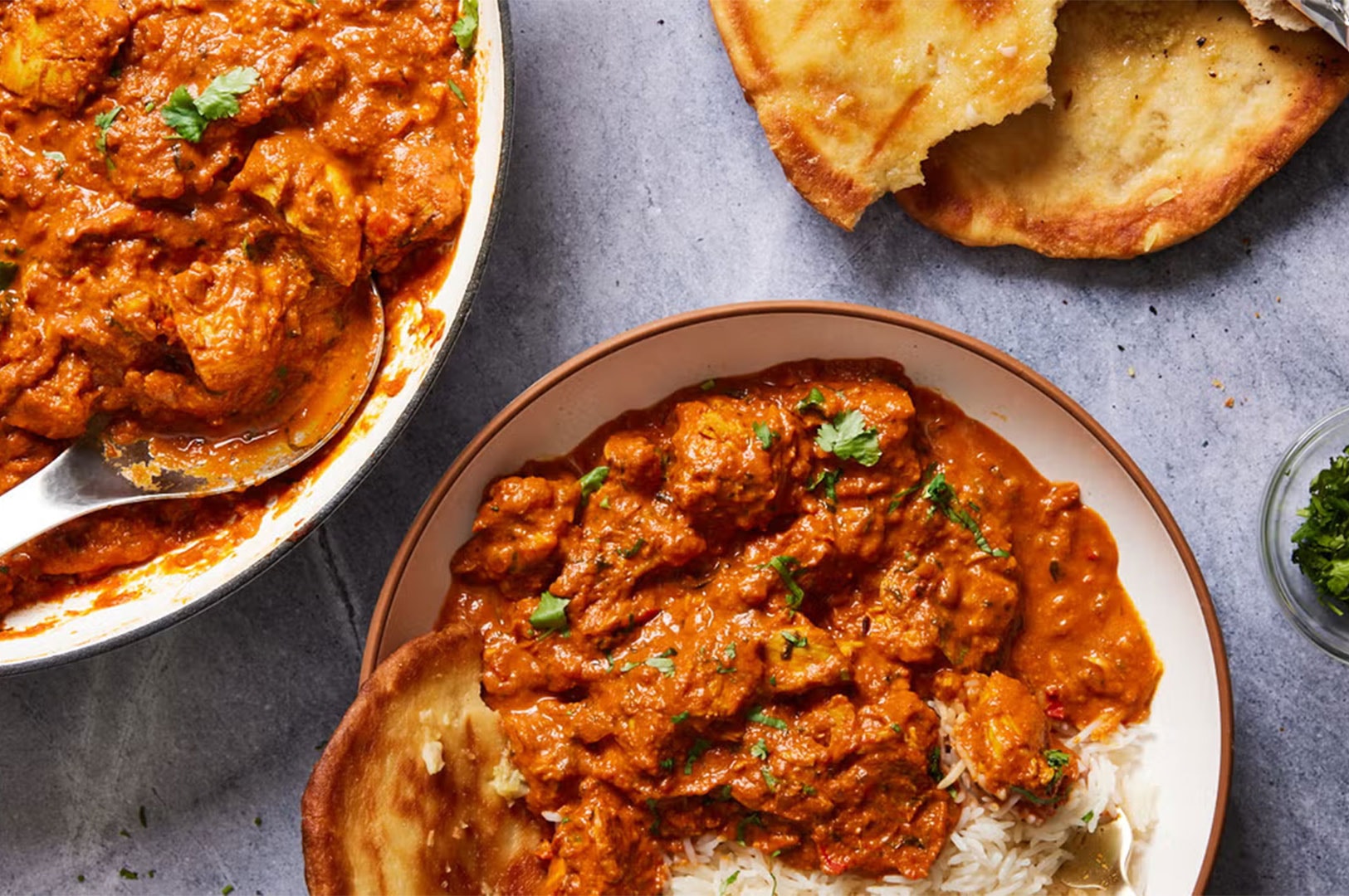 An overhead flat-lay photograph of a home-cooked chicken curry dinner, featuring a serving bowl and skillet of Chicken Tikka Masala over white basmati rice, paired with fresh naan bread.