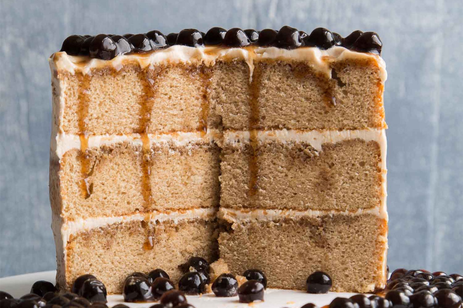 A cross-section of a three-layer milk tea cake featuring brown sugar syrup drizzles and topped with shiny black tapioca pearls.