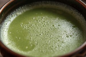 Top-down close-up view of traditional Japanese Matcha green tea with rich green foam in a ceramic bowl.
