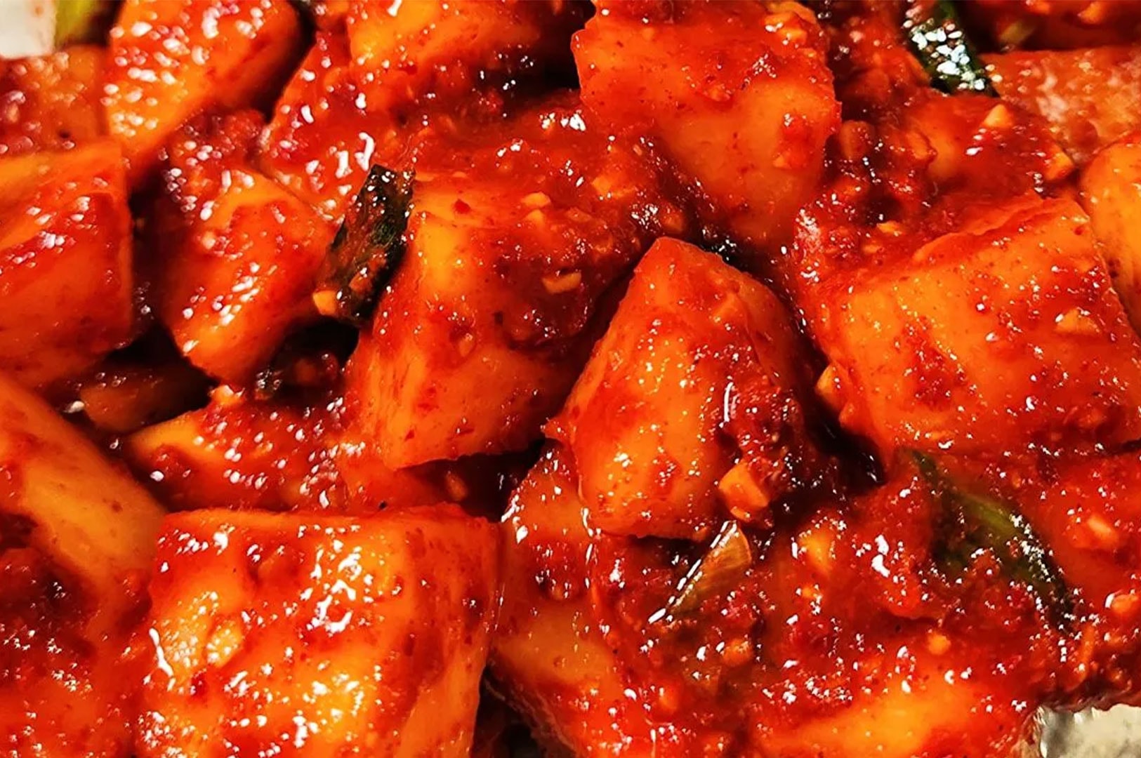 Close-up texture shot of Kkakdugi, a traditional Korean side dish made of crunchy cubed radish fermented in spicy red chili pepper paste.