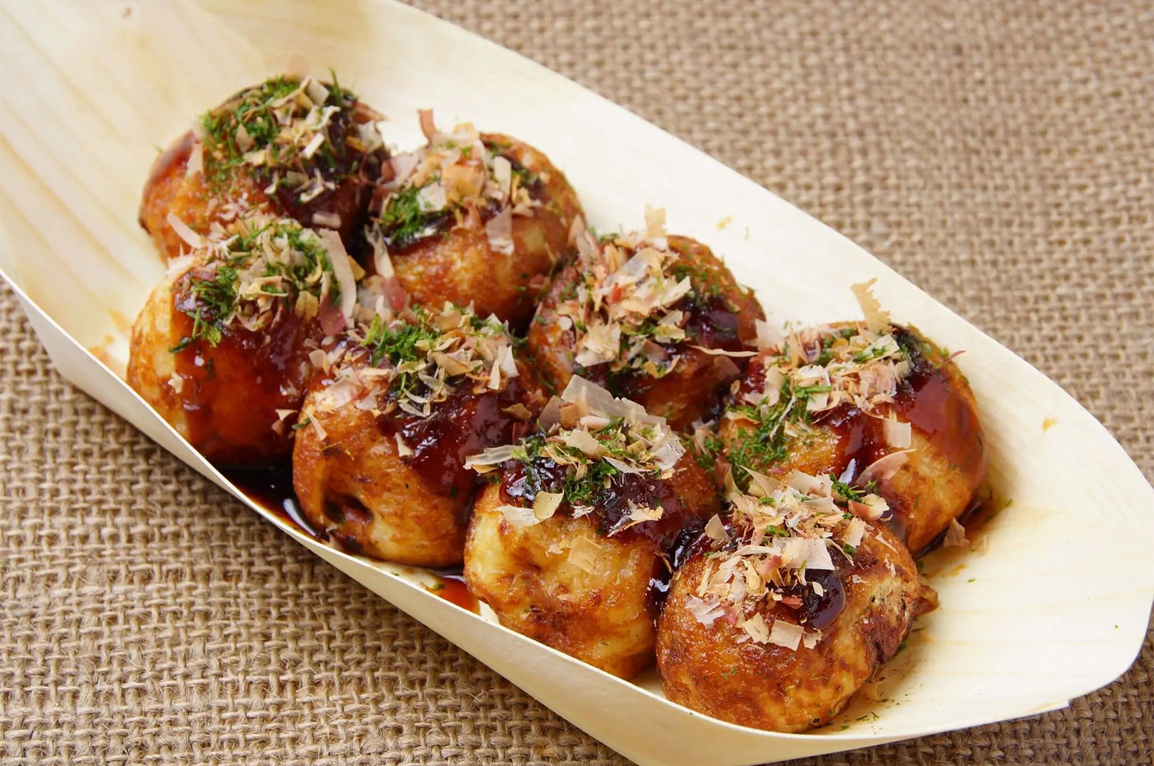 Freshly cooked Japanese octopus balls served in a boat container, heavily topped with savory takoyaki sauce and dried bonito flakes (katsuobushi).