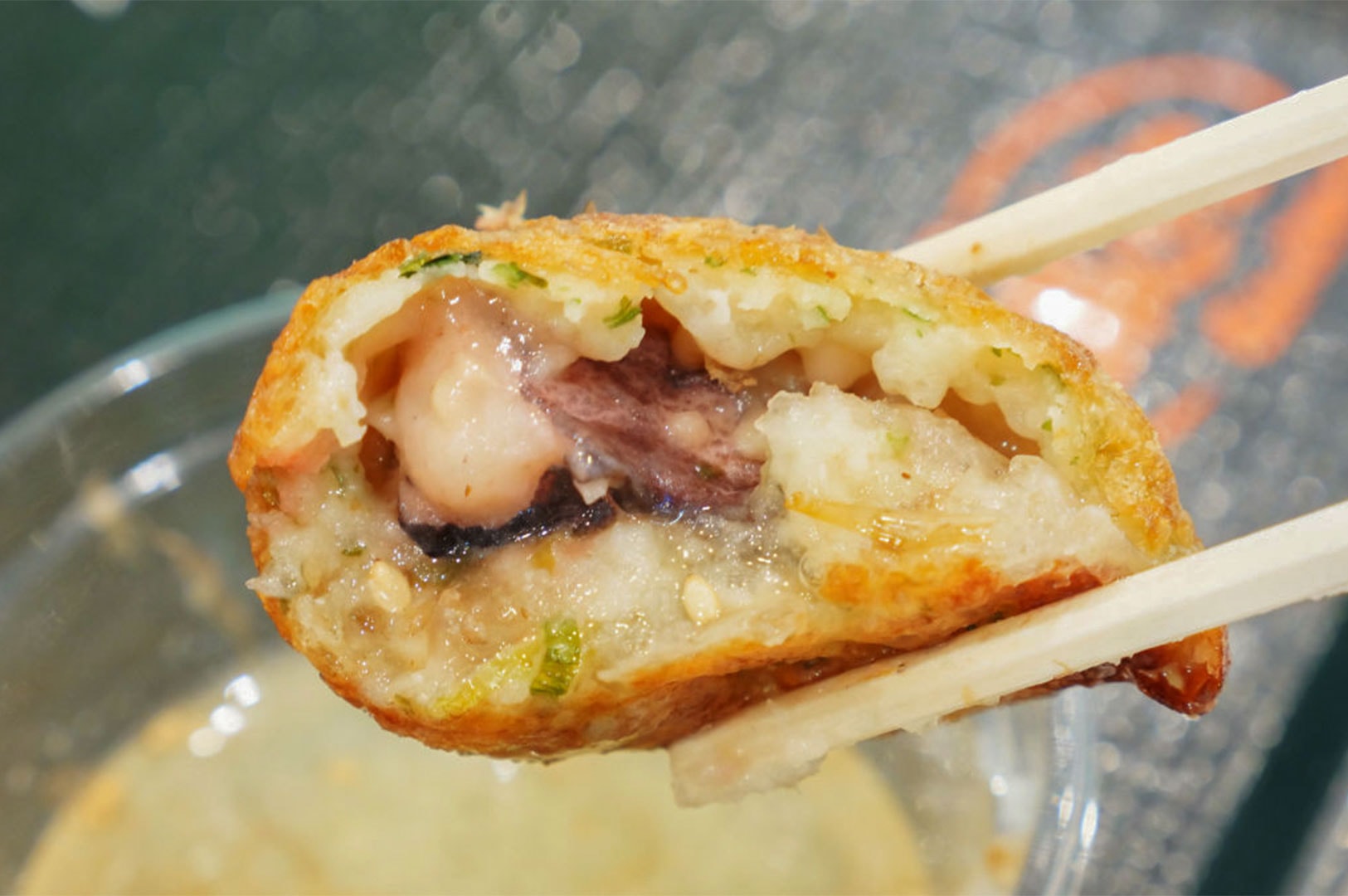 A close-up view of a single takoyaki ball held by chopsticks, bitten open to reveal the large piece of tender octopus and creamy dough inside.
