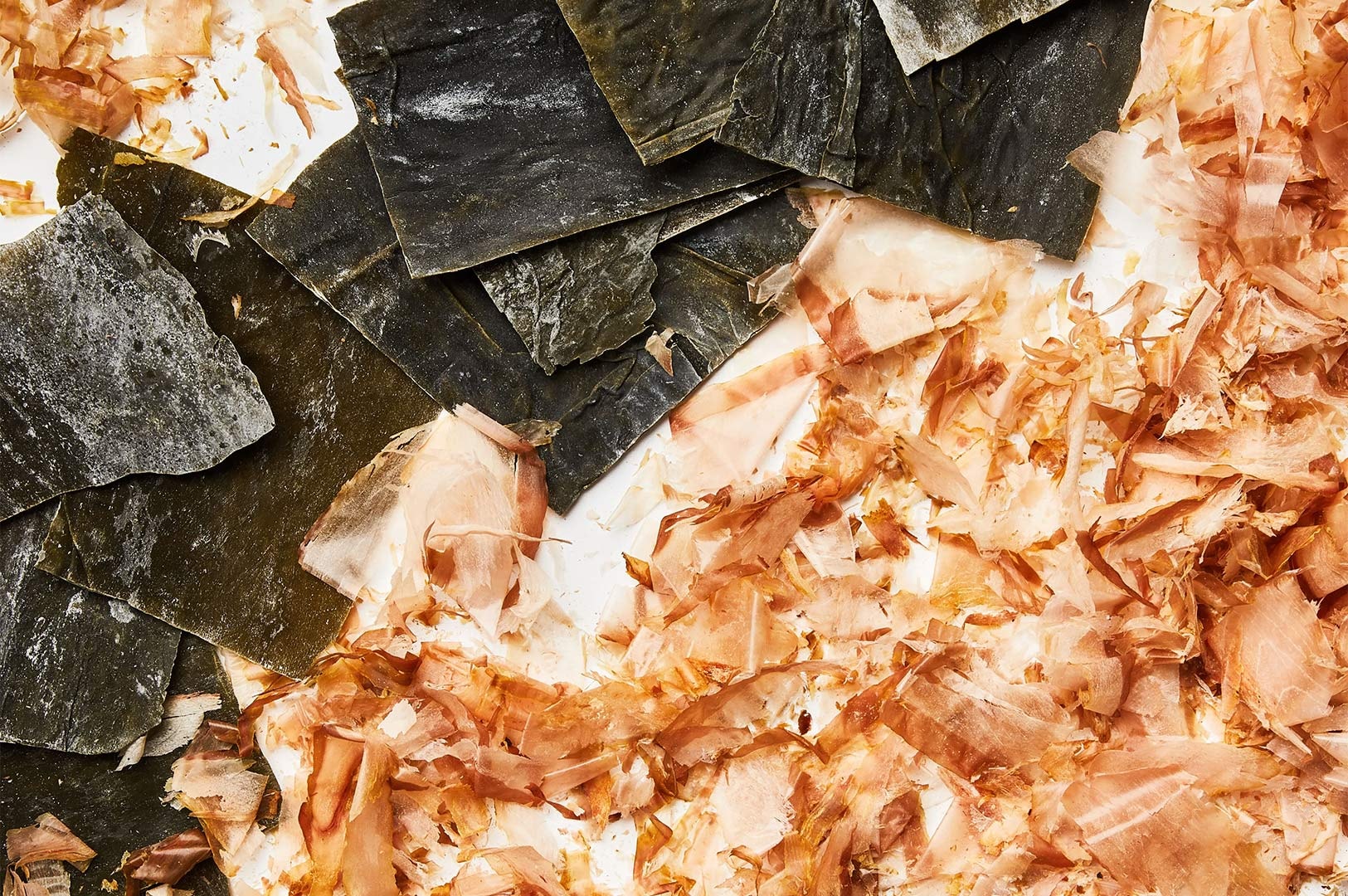 Dried kombu kelp sheets and bonito flakes (katsuobushi) arranged side-by-side, the essential ingredients for making Japanese dashi stock.