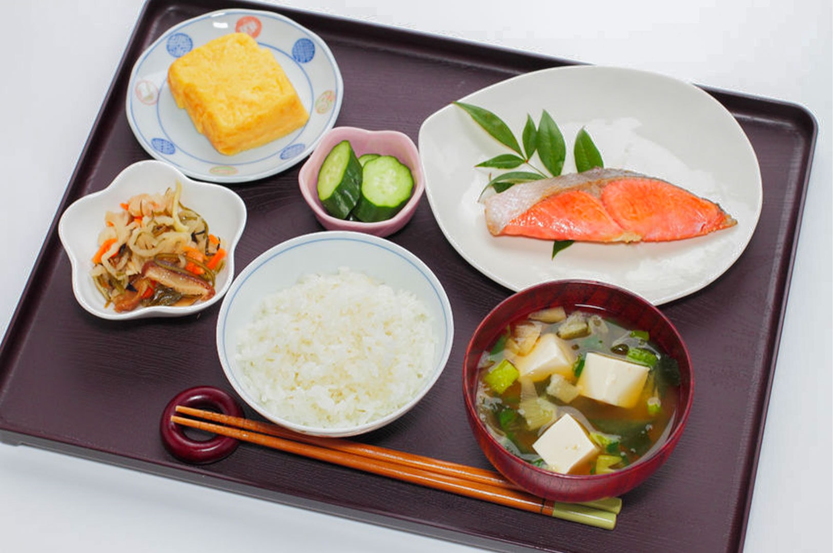 A traditional Japanese breakfast tray (Teishoku) featuring grilled salmon, miso soup, steamed white rice, tamagoyaki omelet, and pickles.