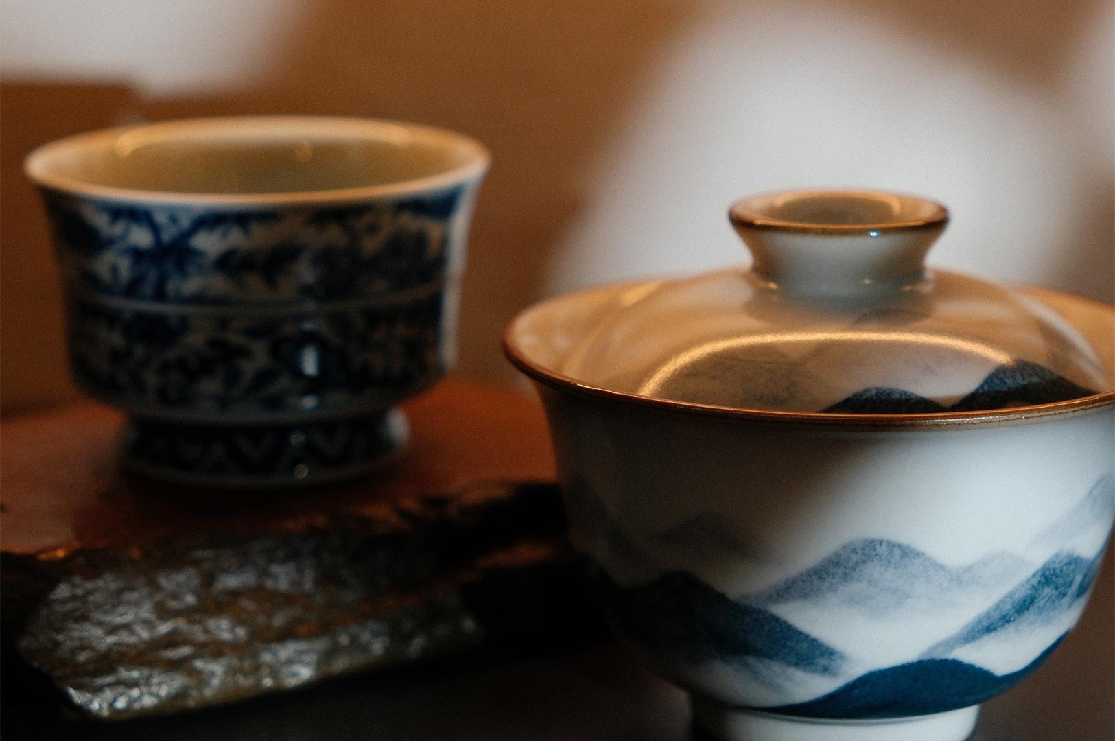Close-up of a traditional Chinese gaiwan and tea cup featuring hand-painted blue mountain landscapes and floral patterns.