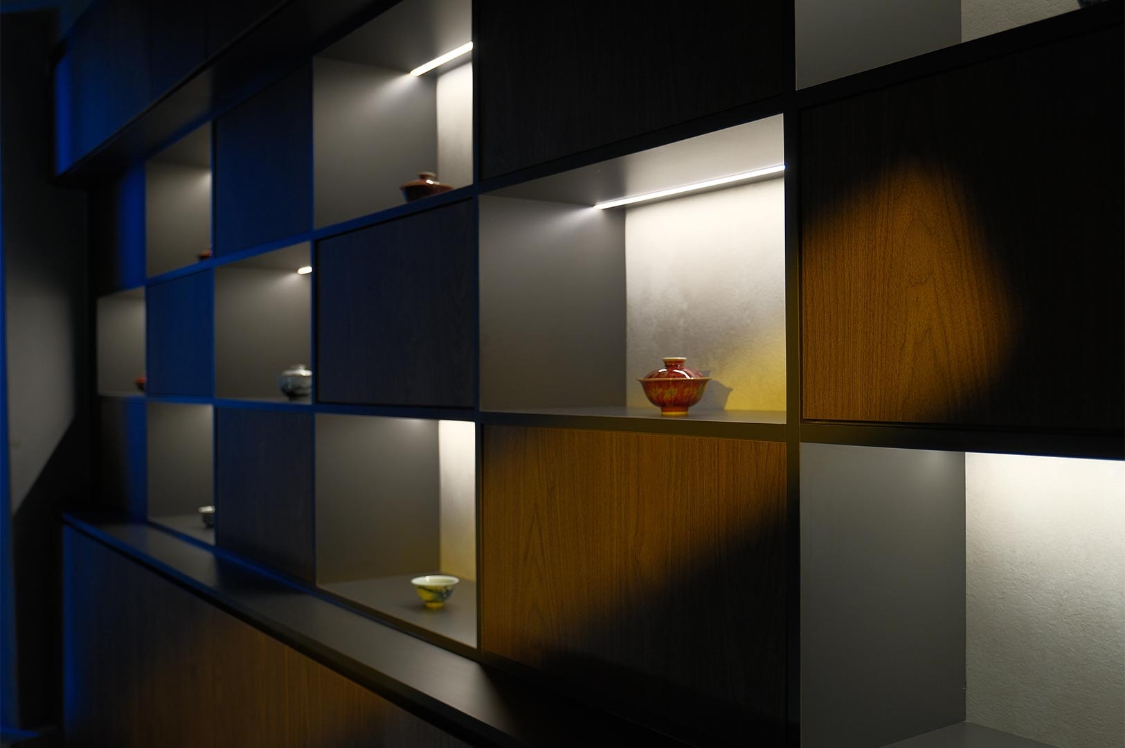 A modern dark wood grid display cabinet with integrated LED strip lighting showcasing various artisanal ceramic tea bowls.