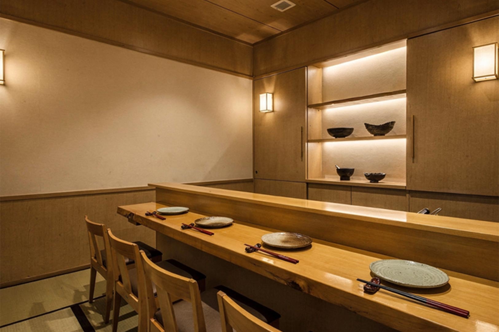 An empty, elegant Japanese sushi bar with light wood finishes, individual place settings, and warm ambient lighting.