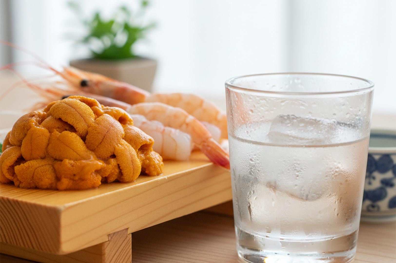 A close-up of premium bright orange uni (sea urchin) and raw sweet shrimp served on a wooden geta block next to a glass of water.