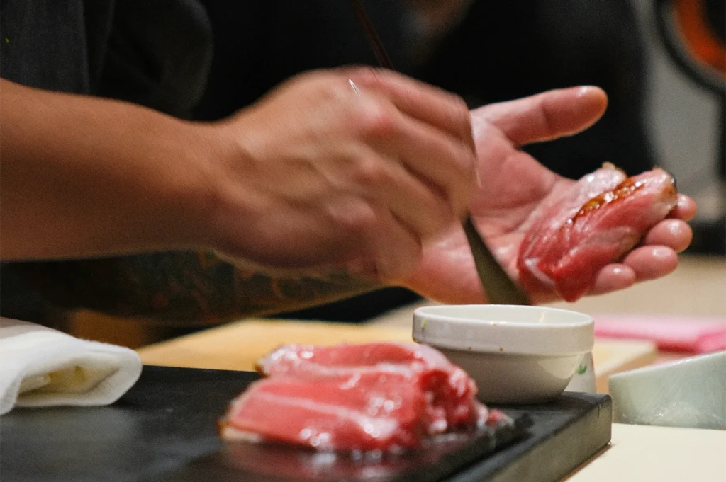 Close-up of a sushi chef using a brush to apply nikiri soy glaze to a piece of fatty tuna (toro) nigiri.